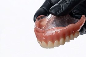 Hand in black glove holding denture for upper arch