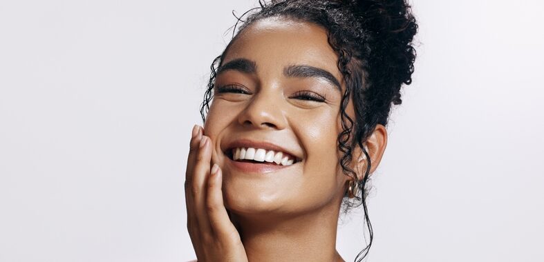 Smiling young woman with curly hair touching her cheek