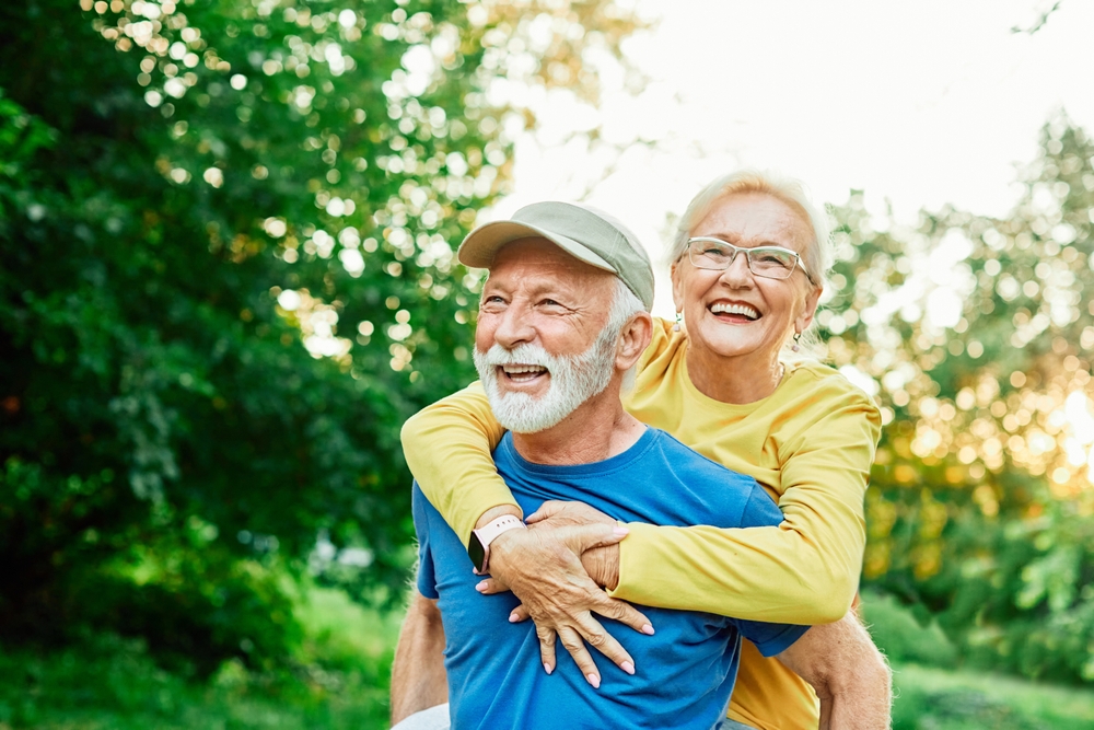 Senior man in a cap giving his wife a piggyback ride in a park